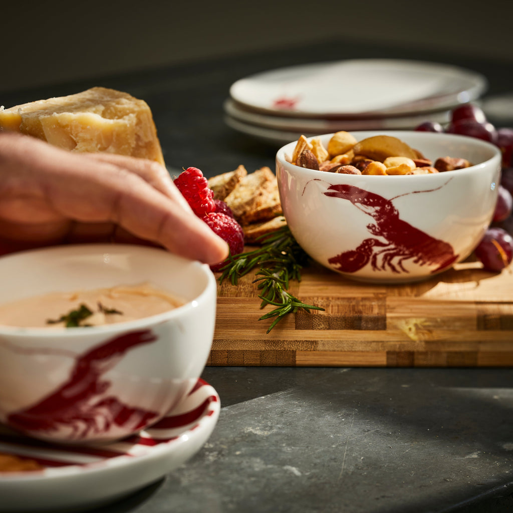 A Red Lobster Snack Bowl from Caskata holds nuts on a wooden charcuterie board.