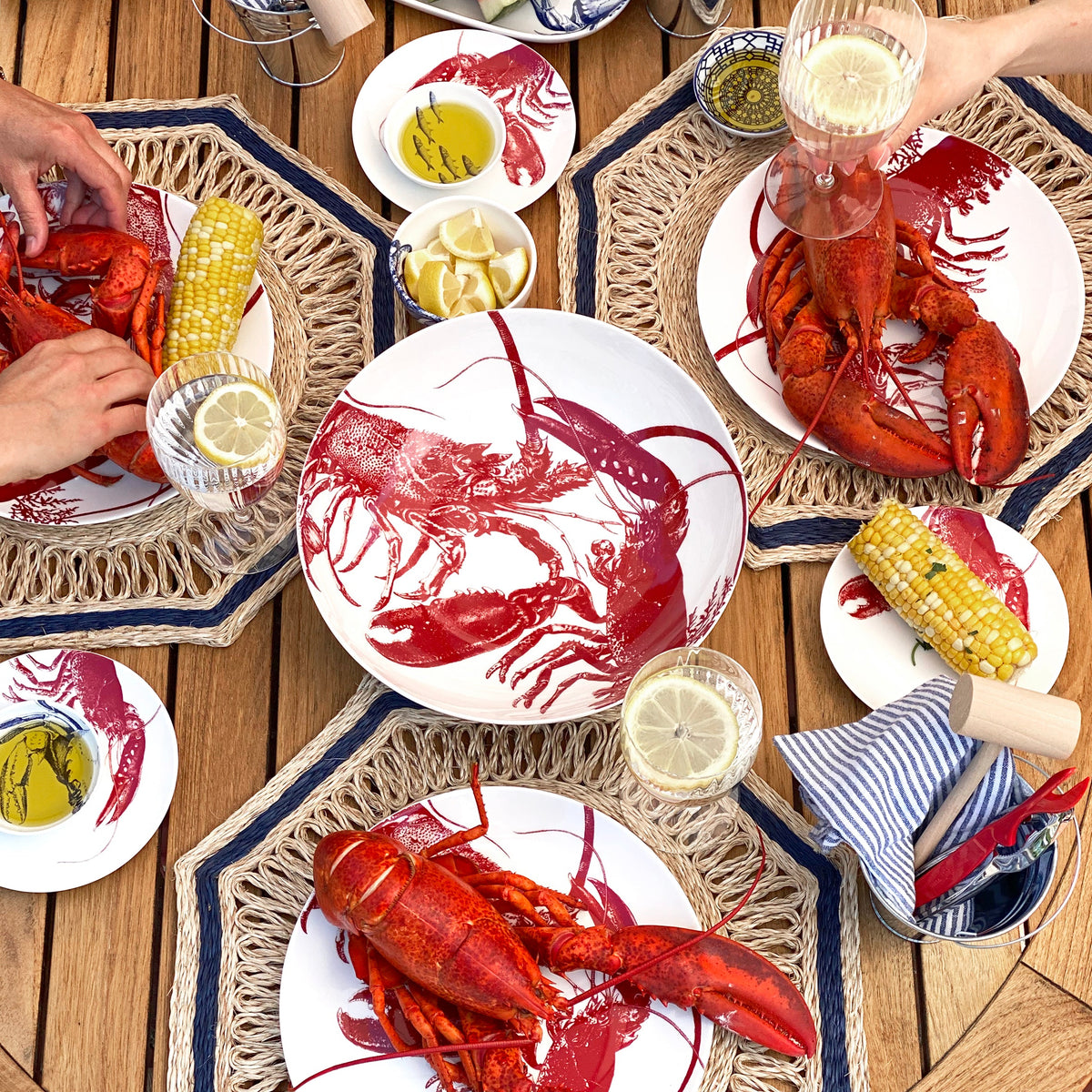 A group of people enjoying seaside dining with lobsters on Red Lobster Canapé Plates by Caskata Artisanal Home.