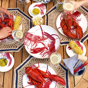 A group of people enjoying seaside dining with lobsters on Red Lobster Canapé Plates by Caskata Artisanal Home.