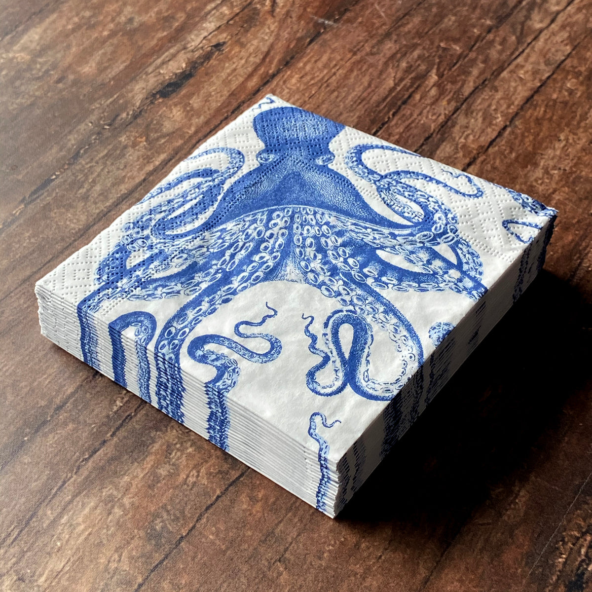 Angled view of Lucy Cocktail Napkins showcasing blue octopus pattern on a white stack over a wood surface