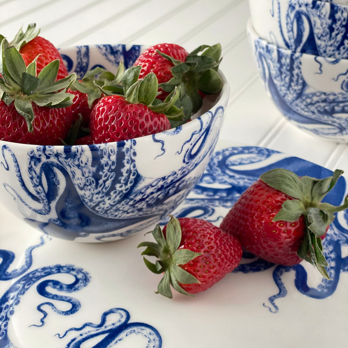 Close-up of Blue Lucy Tall Cereal Bowl showcasing blue octopus pattern with strawberries on a white table