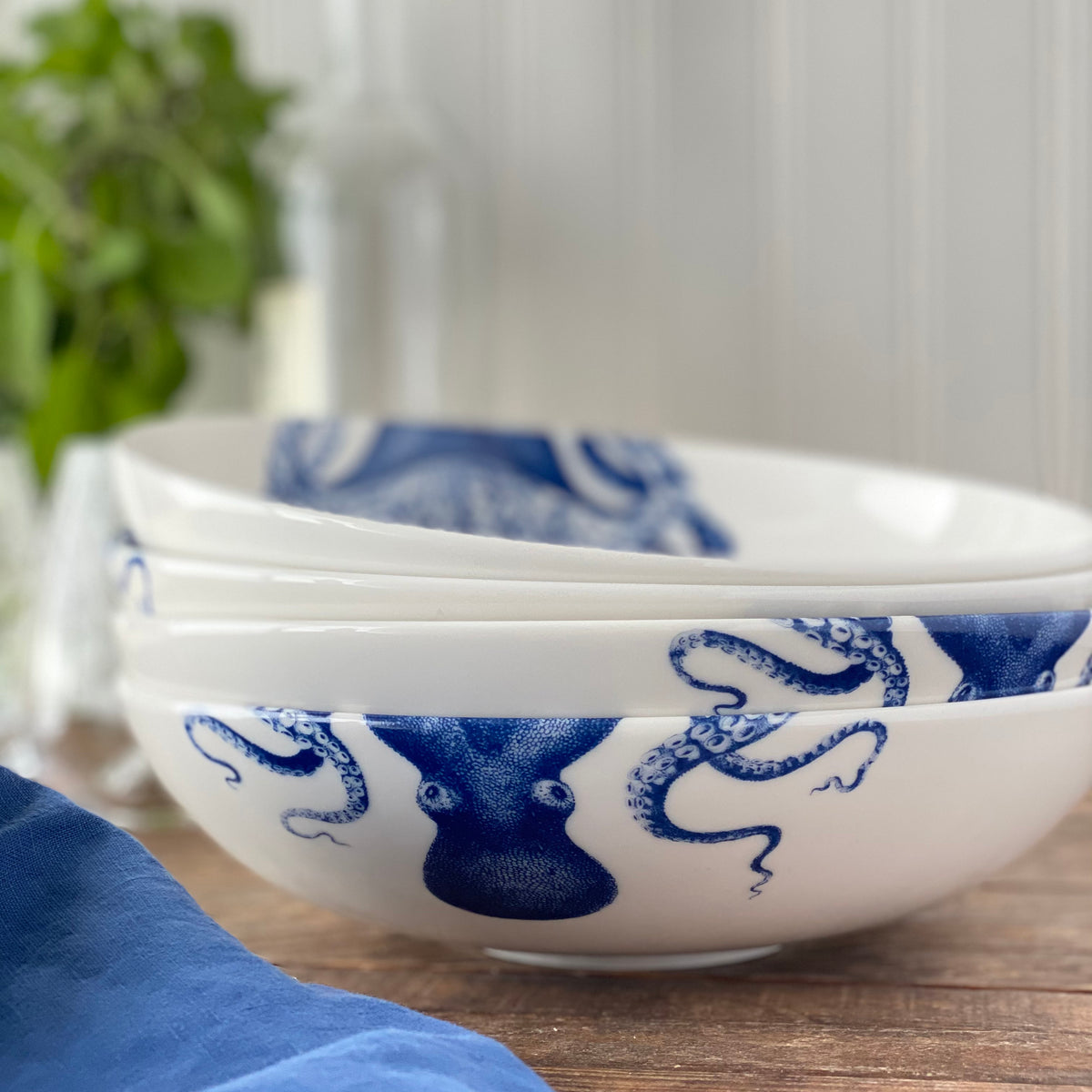 Close-up view of Blue Lucy Wide Serving Bowl showcasing blue cephalopod pattern with a blurred plant background