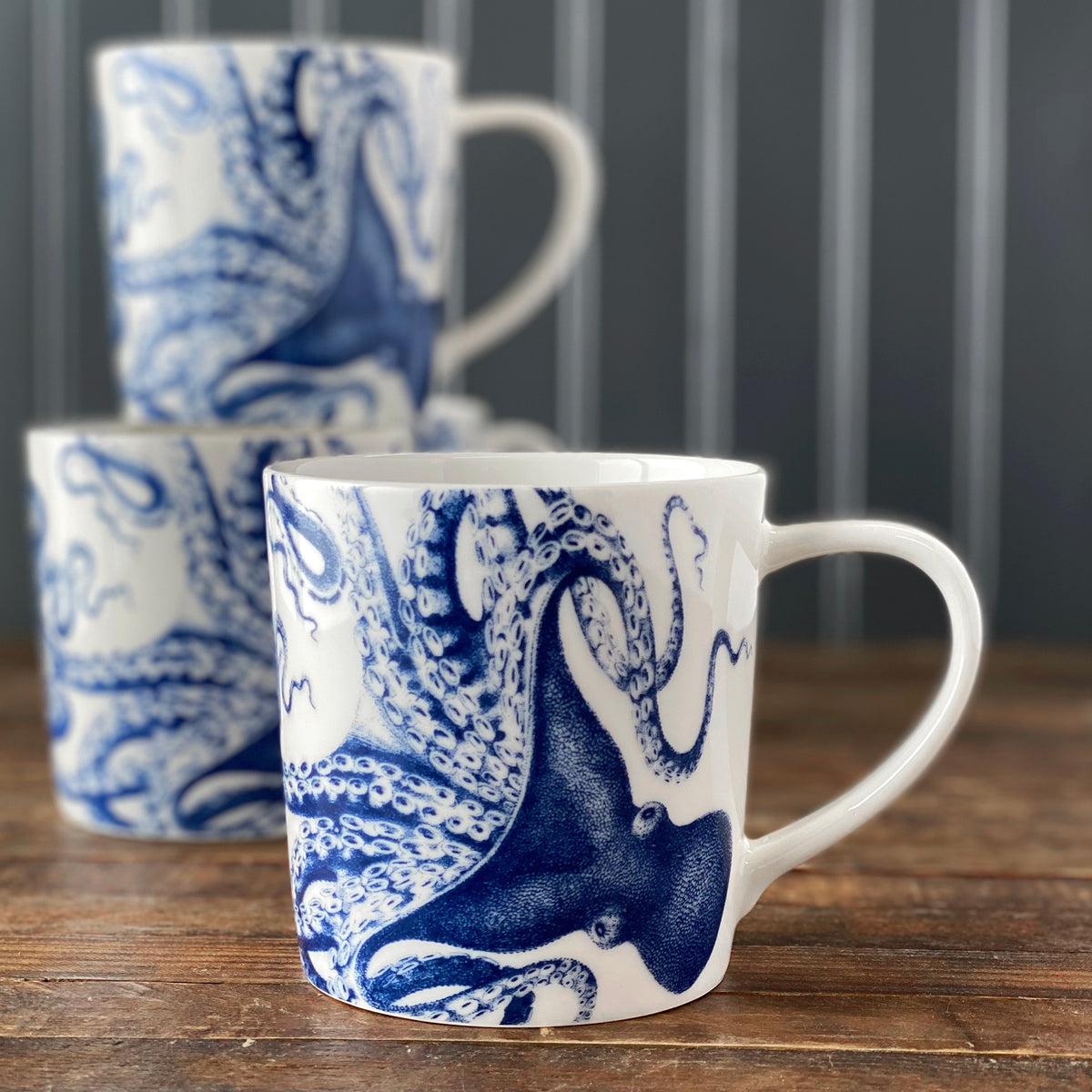Front view of Lucy Mug in Blue showcasing a blue cephalopod design with another mug on a wooden tabletop