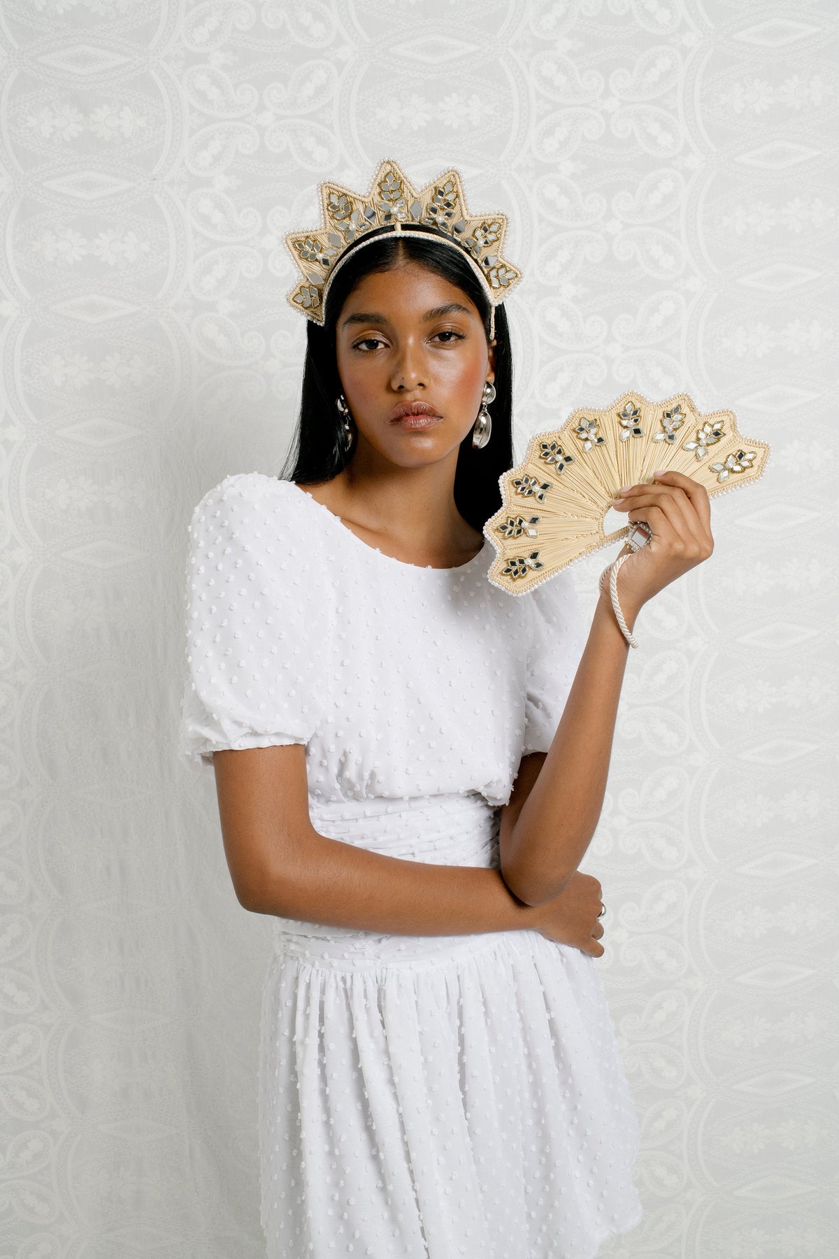 Model wearing the Star Shaped Iraca Jaipur Mirror Headpiece while holding an embellished fan against a white patterned backdrop