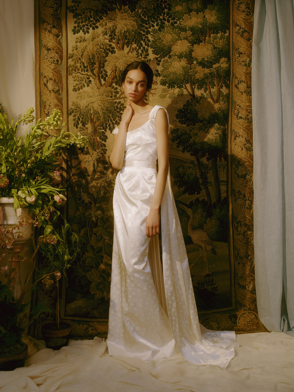 Front view of white floral ditsy print gown showcasing corset bodice and shoulder strap trains with floral tapestry background