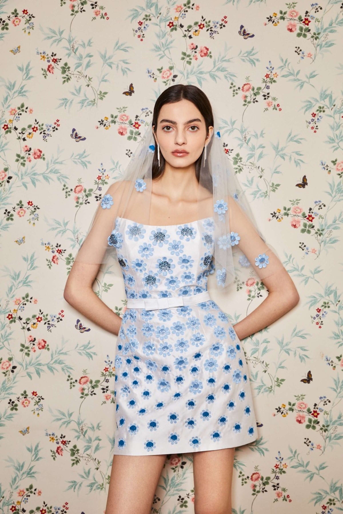 Front view of Lulu White Silk Mini Dress showcasing blue daisy embroidery and white bow belt against floral backdrop