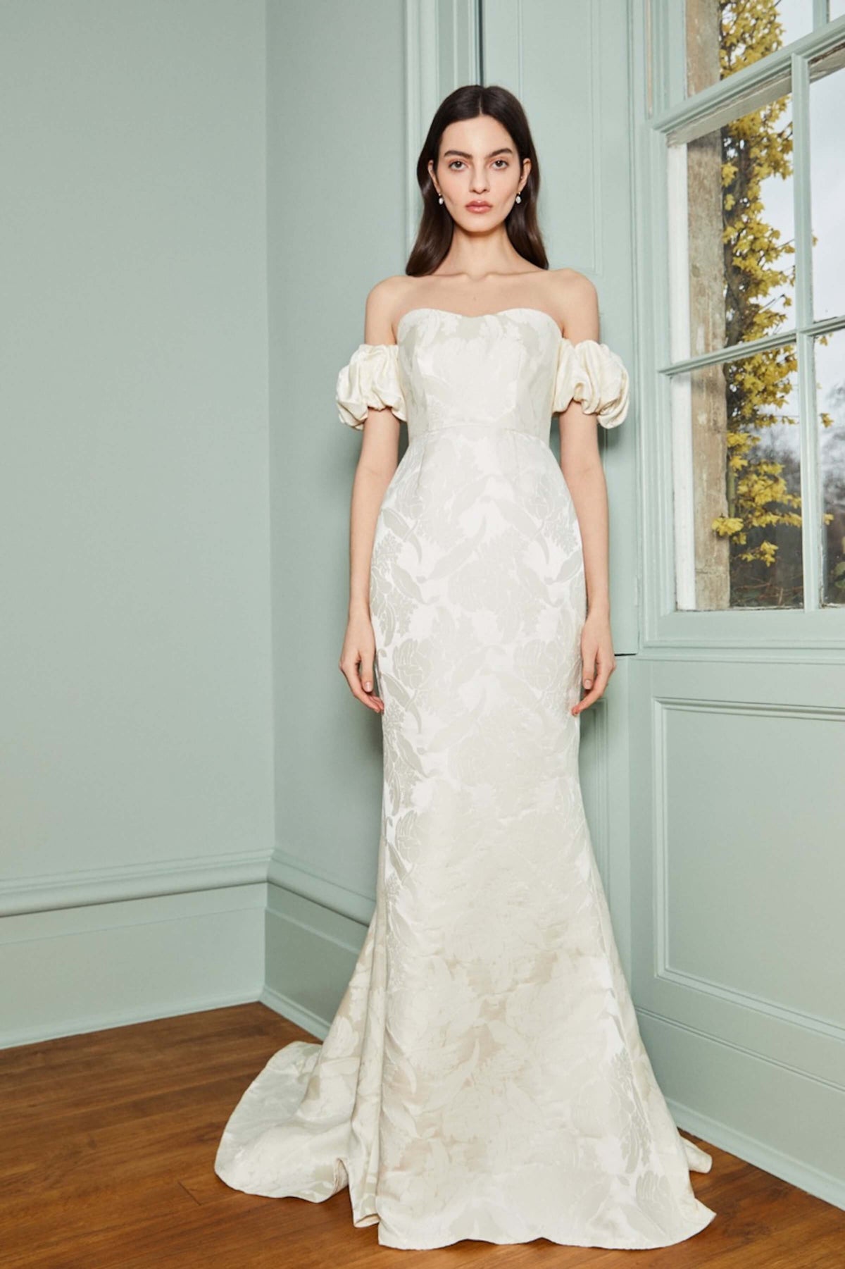 Front view of Luisa white floral jacquard gown showcasing sweetheart off-the-shoulder neckline and puff sleeves in green room