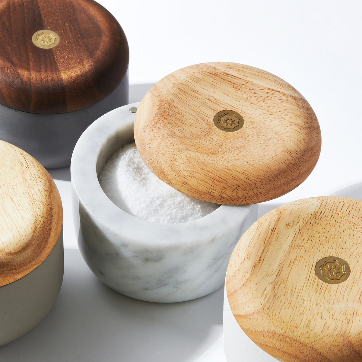 Close-up of Evermill Salt Well showcasing an open white marble salt cellar with a light wood lid and brass emblem on a white background