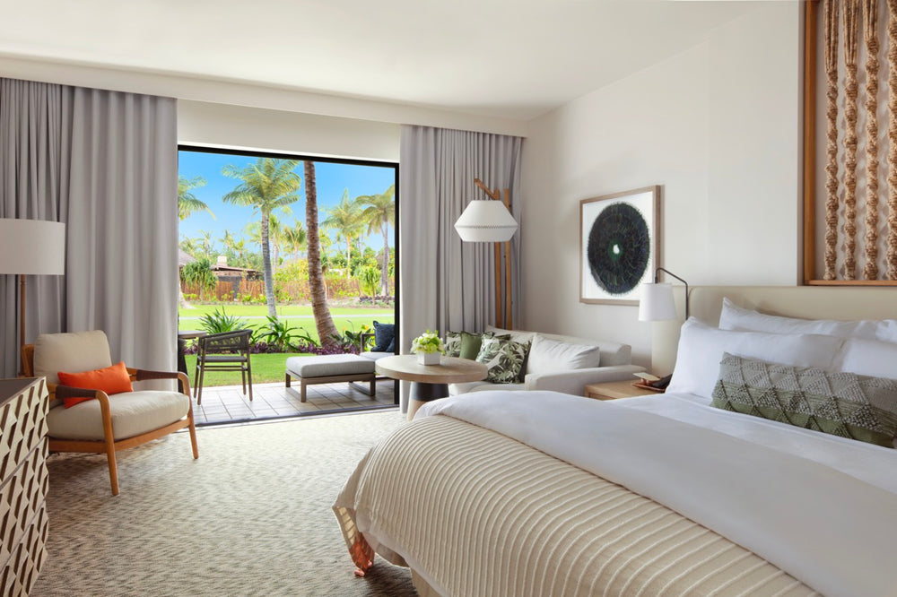 Front view of Mauna Lani garden-view guestroom showing king bed, seating area, and sliding patio opening to a palm-lined lawn