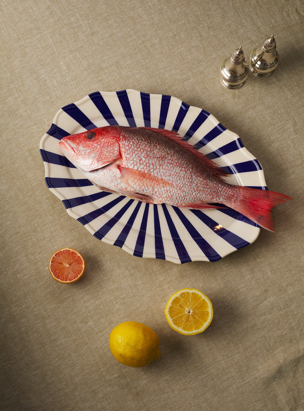 Top view of Mafalda Oval Platter showcasing blue-and-white radial stripes and scalloped edge on a neutral linen tablecloth