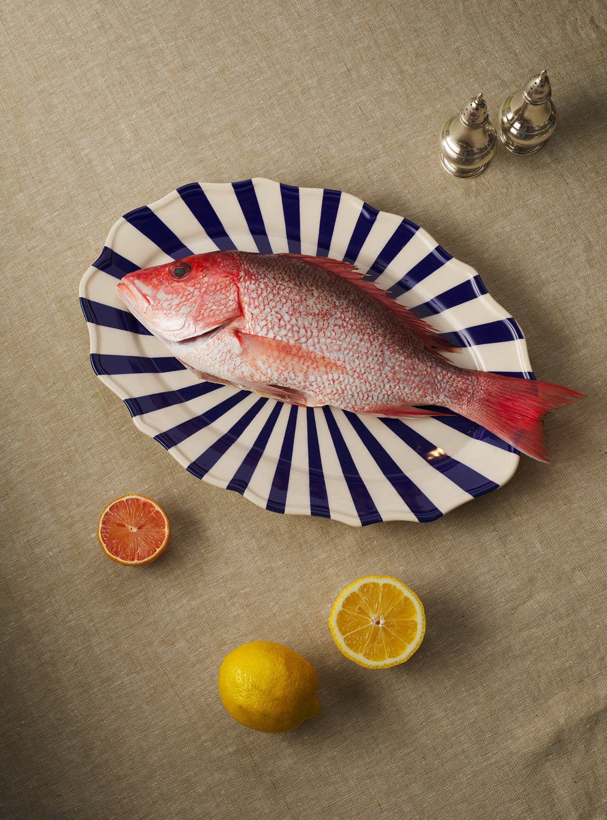 Top view of Mafalda Oval Platter showcasing blue-and-white radial stripes and scalloped edge on a neutral linen tablecloth