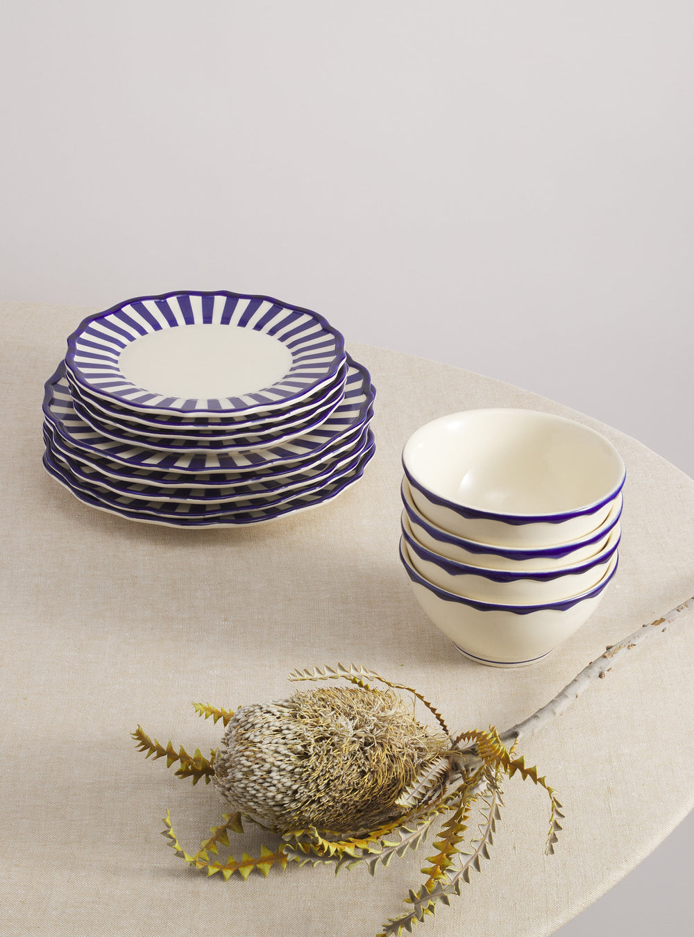 Riviera 12-piece dinnerware set, stacked plates and four cereal bowls with blue scalloped striped rims on beige table