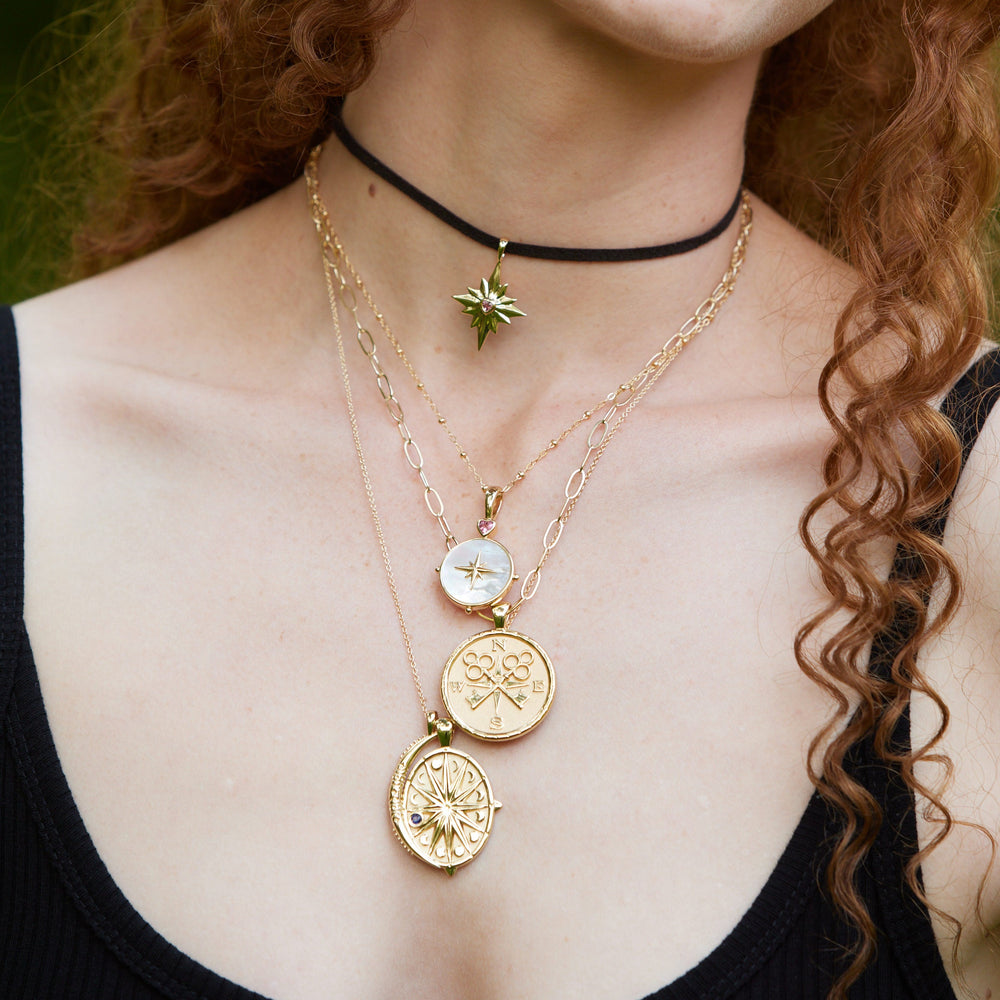 Close up of layered Forever Make A Wish birthstone star necklace with gold compass and mother of pearl charms