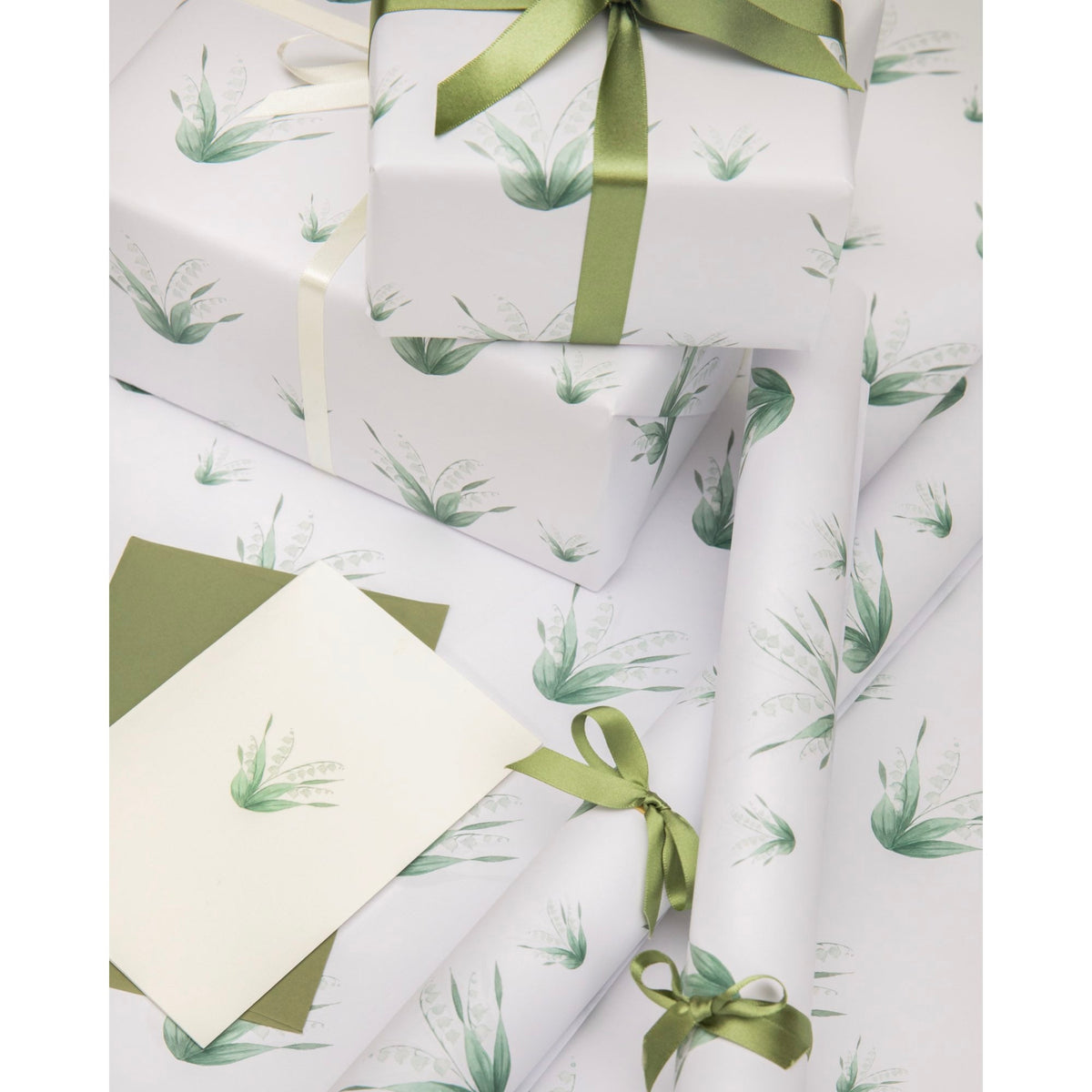 Flat lay of Lily of the Valley wrapping paper with green floral sprigs on white and wrapped gifts with green ribbons