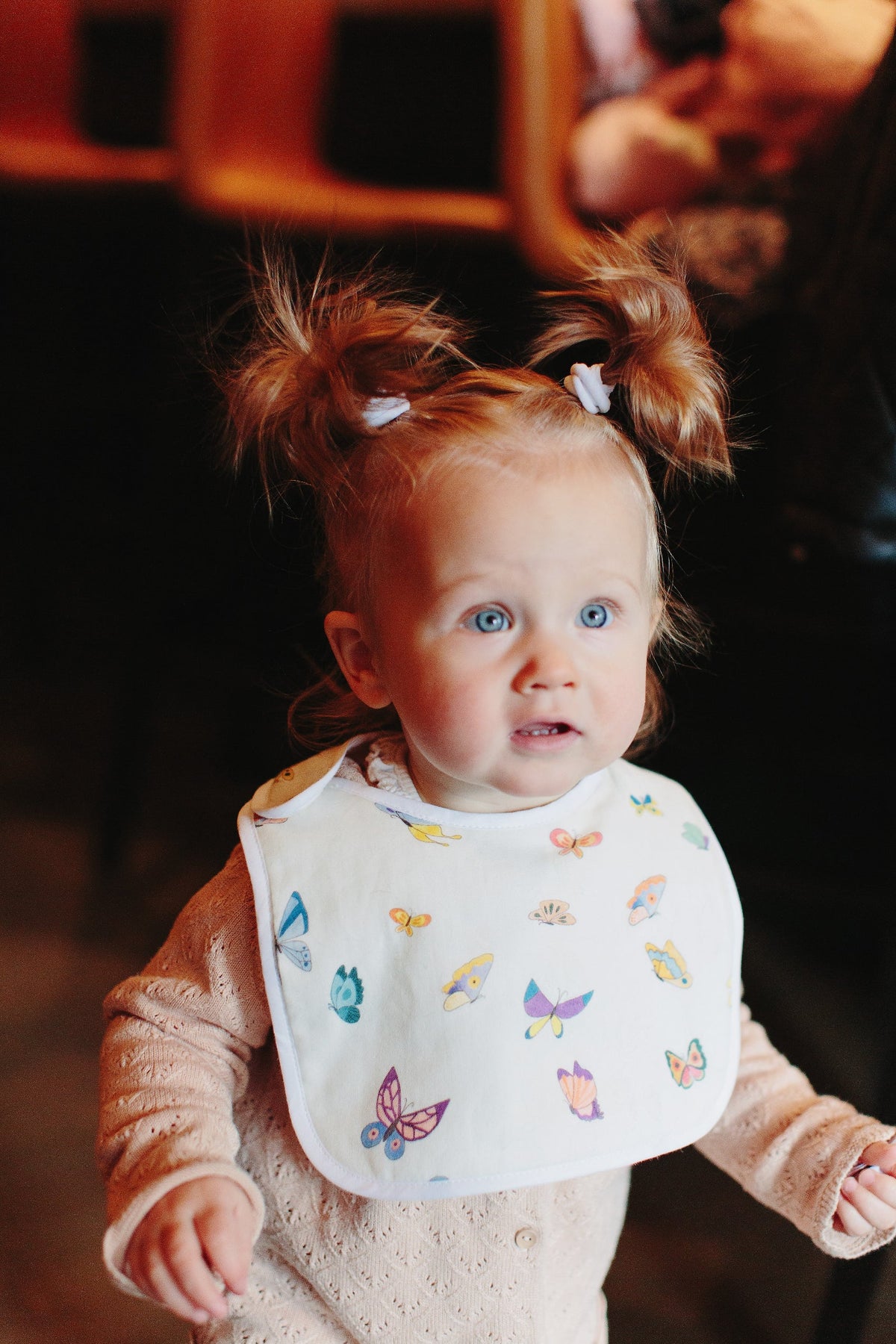 Front view of Madame Butterfly bib showing colorful butterfly print on white muslin with piped edge