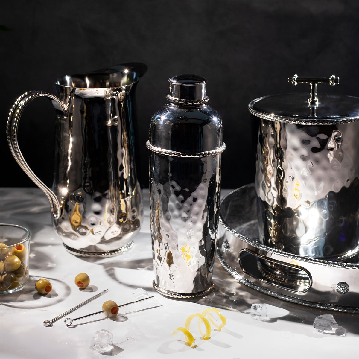Three-quarter view of Graham Silver Pitcher showcasing hammered polished stainless steel finish and rope-detail handle on a dark backdrop