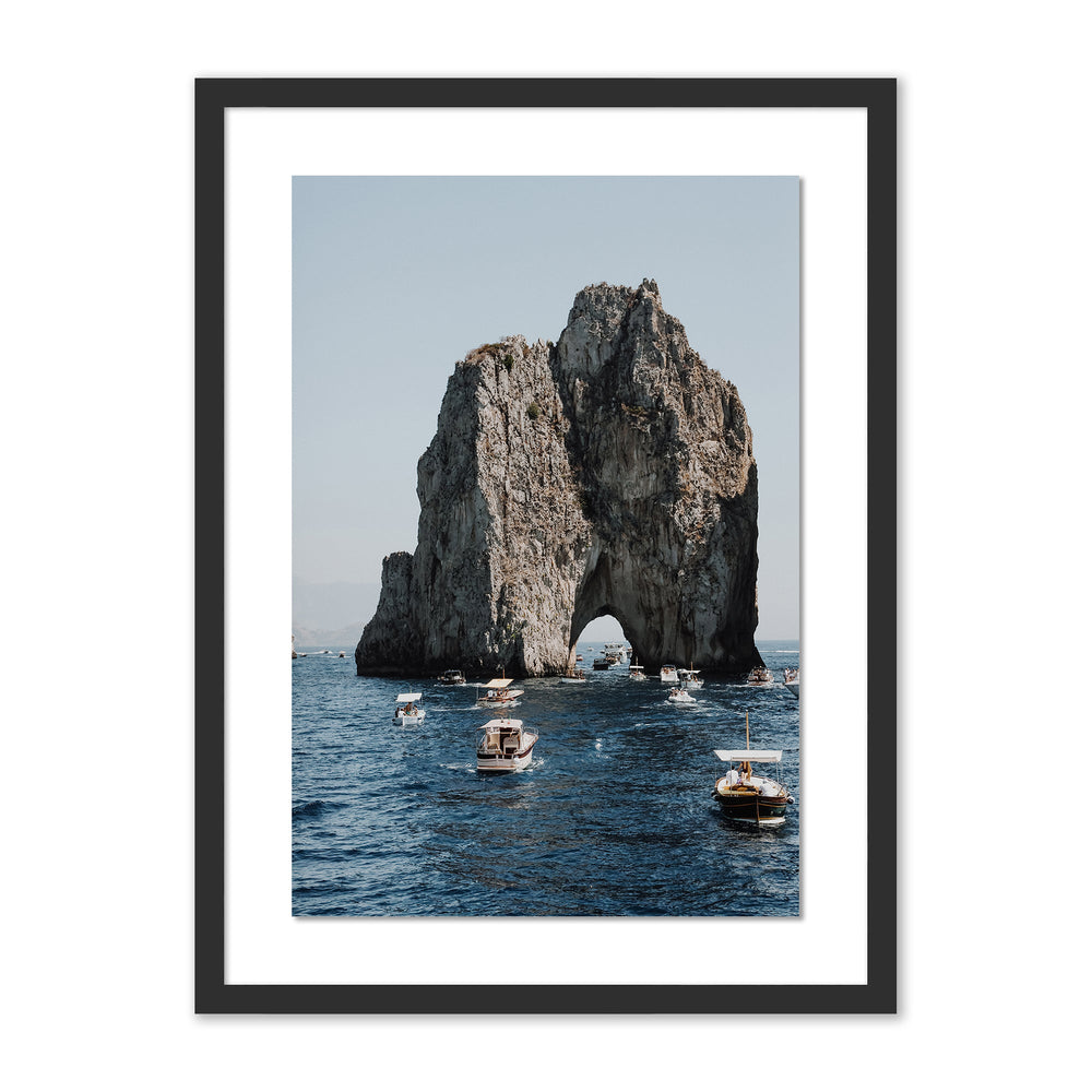 Front view of Commute To Pasta print showcasing a rocky sea arch with several small boats on deep blue water and a pale sky