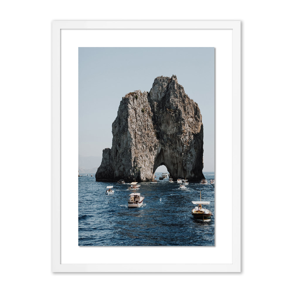Front view of Commute To Pasta framed print showing a large rocky sea arch with several small boats on deep blue water