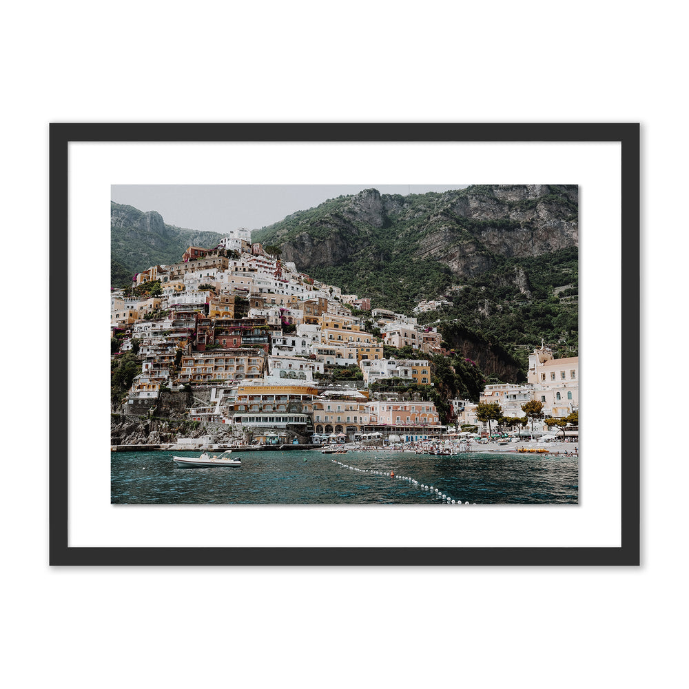 Front view of The Money Shot print showing pastel cliffside buildings above turquoise sea, framed with white mat and black frame