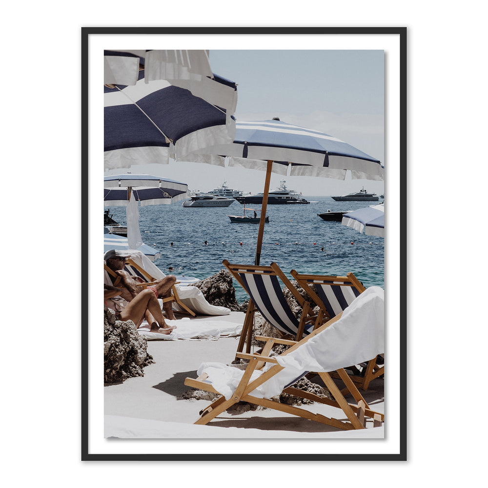 Front view of framed Blue and White Print showing blue-and-white striped beach umbrellas, wooden deck chairs, and yachts on the sea