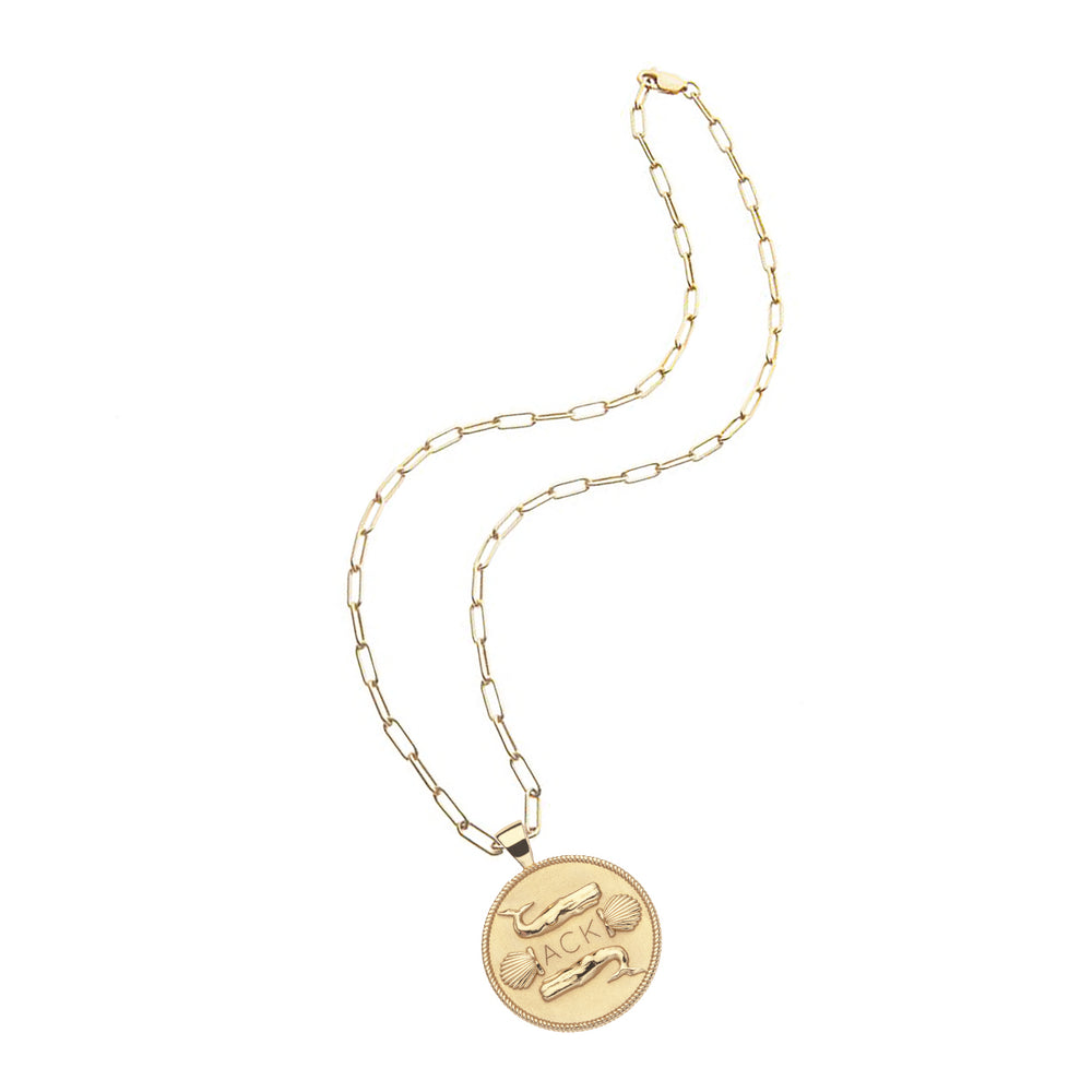 Flat lay of Nantucket JW Original pendant coin necklace showcasing gold-dipped coin engraved with whales and shells on a white background