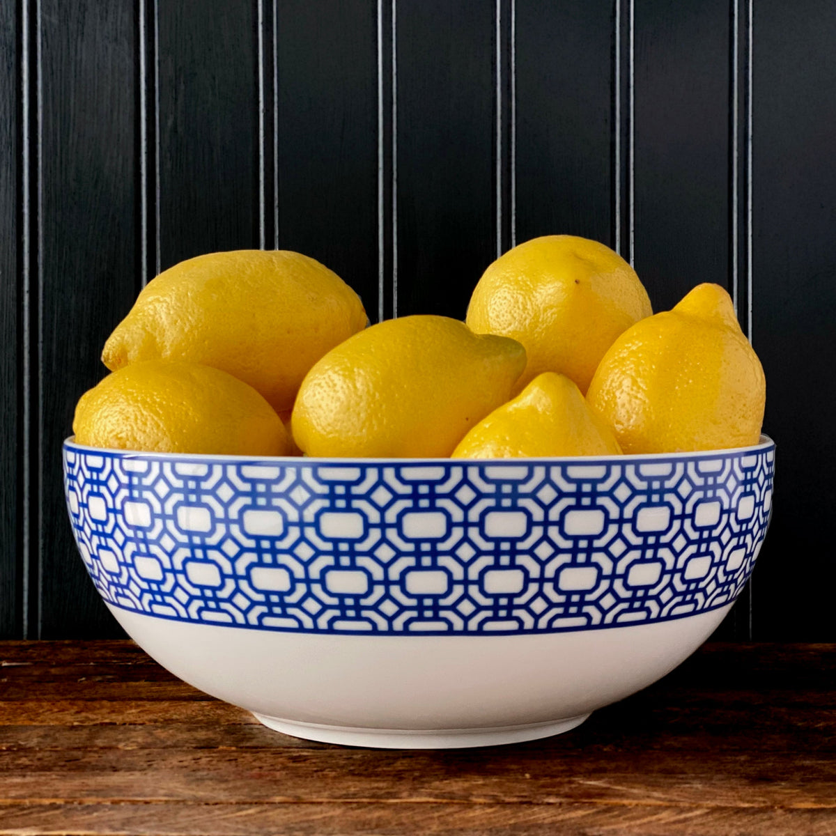 Side view of Newport Garden Gate serving bowl showcasing blue geometric border filled with lemons on dark paneled background