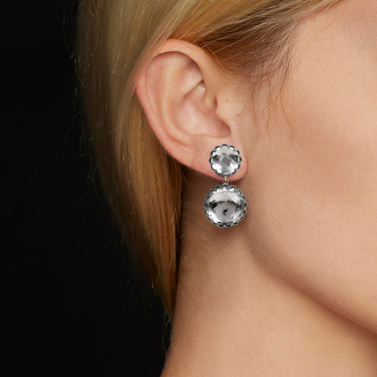 Close-up view of Olivia Small Day Night Earrings showcasing 28 ct white quartz drops worn on an ear against a black background