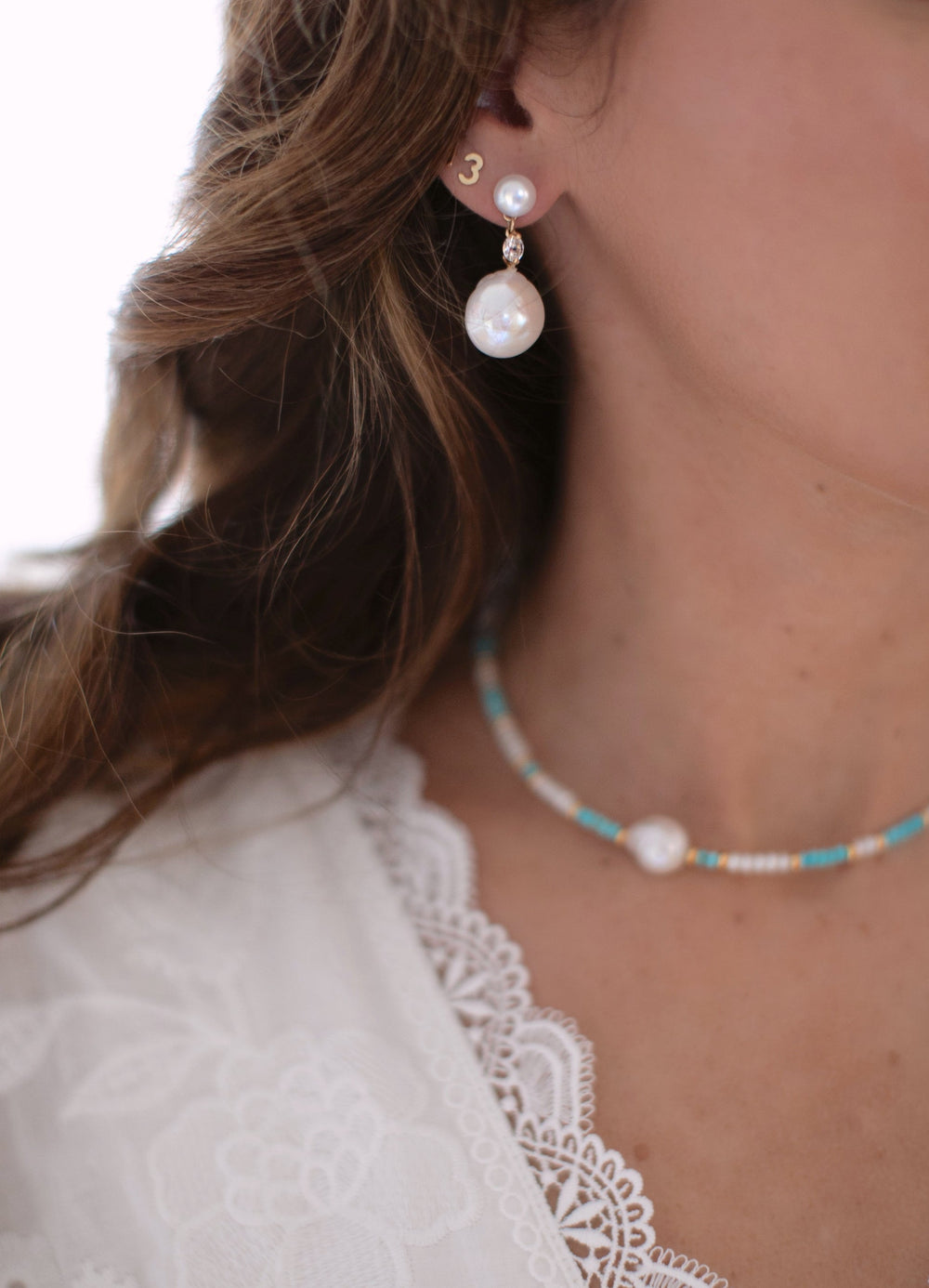 Side view of October Earrings showing pearl stud, white topaz connector, and baroque freshwater pearl drop against lace blouse