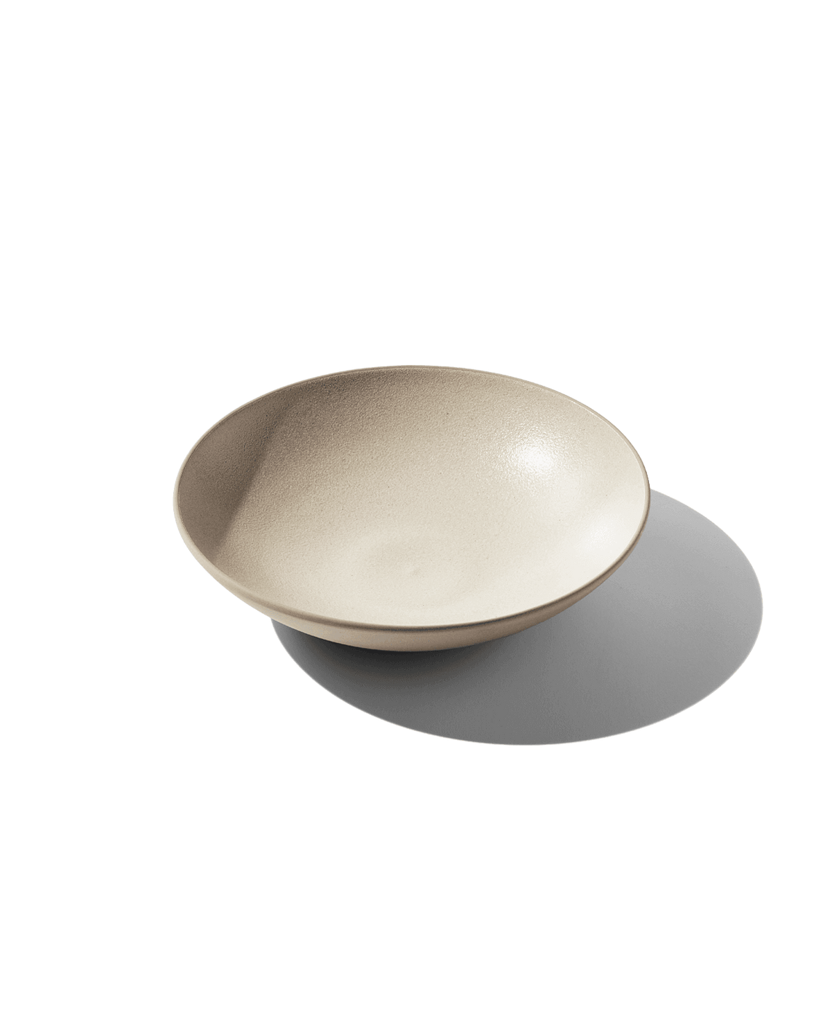 Three-quarter view of The Open Bowl showcasing its shallow, wide shape and hand-finished Korean clay with a green background