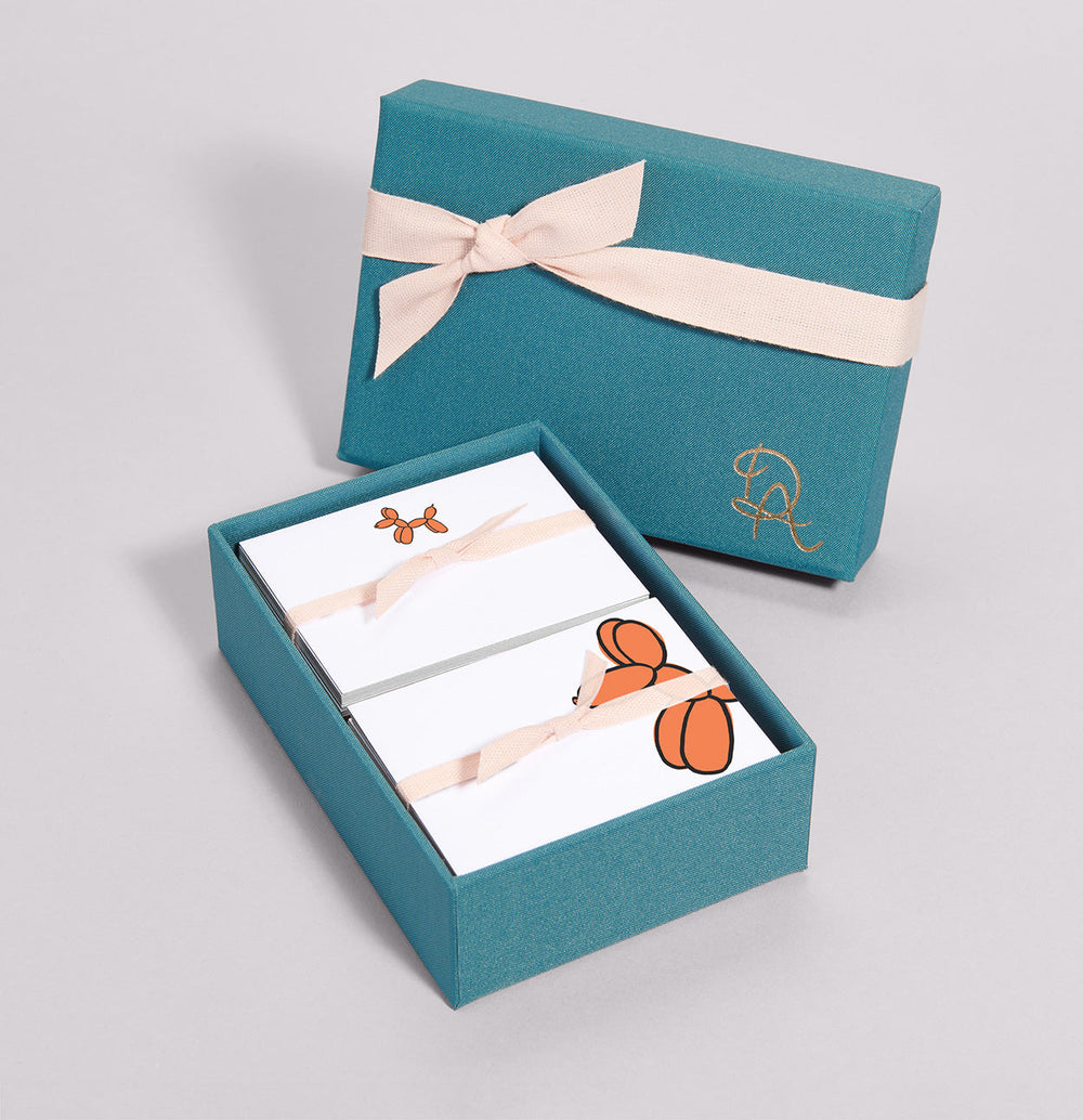 Angled Party Animals place card set in teal box showing cards with orange balloon dog illustrations and pink ribbon on gray