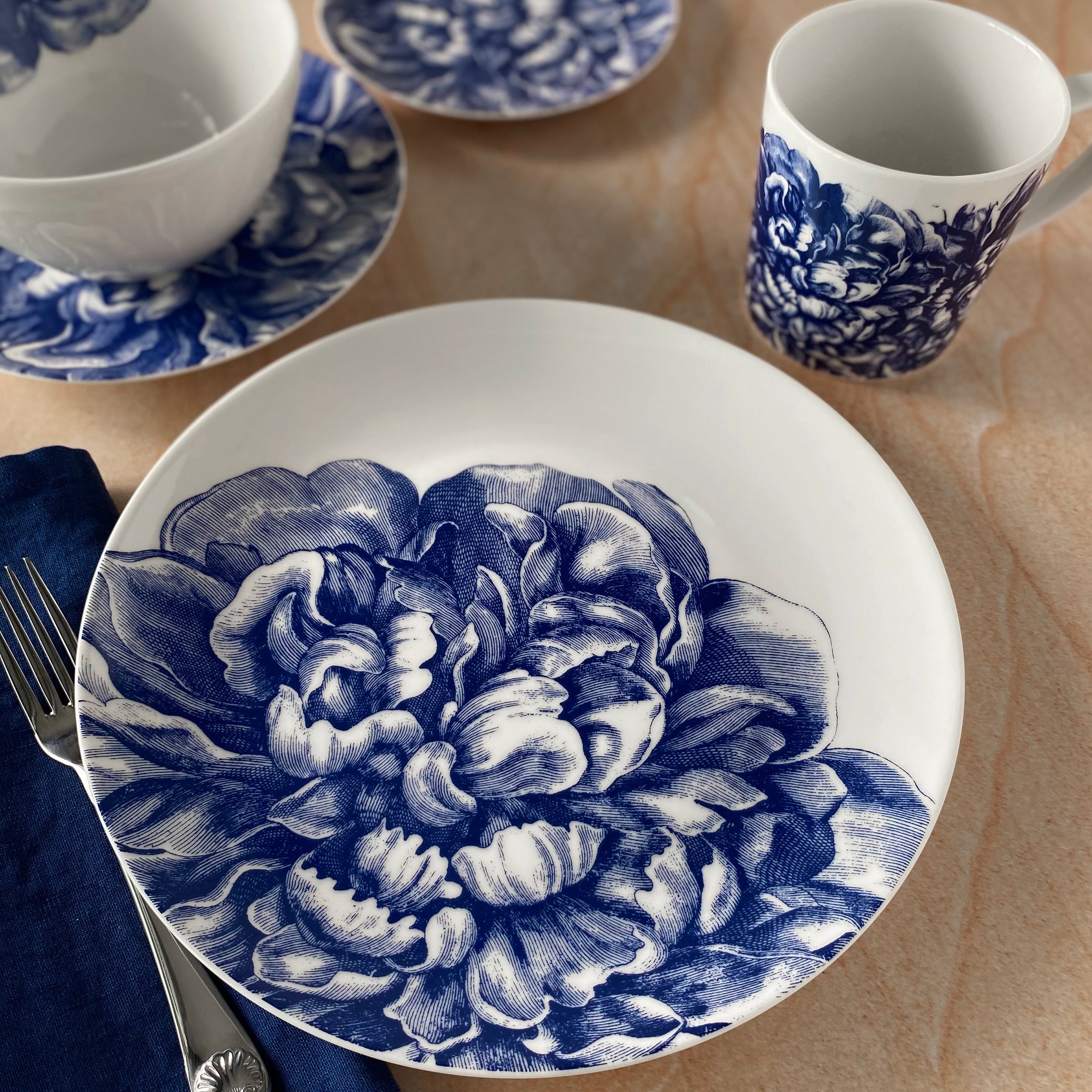 A set of Caskata Artisanal Home's Peony Blue 4-Piece Place Setting, featuring peony blossoms beautifully arranged on a table.