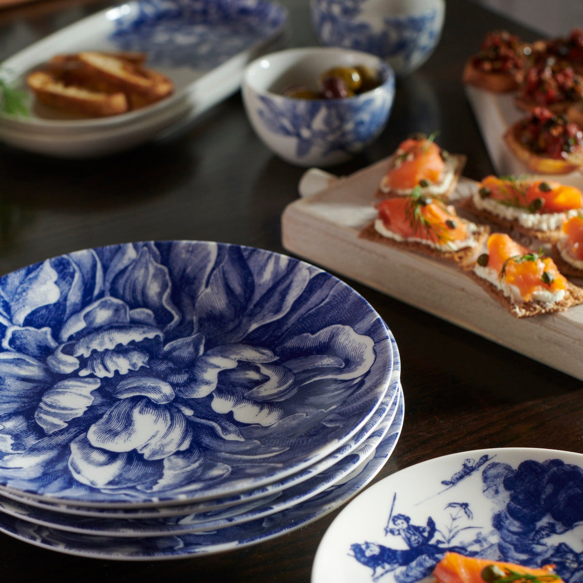 A set of Peony Blue 4-Piece Place Setting by Caskata Artisanal Home, featuring a beautiful blue and white theme, adorned with delicate peony blossoms, elegantly arranged on a table.