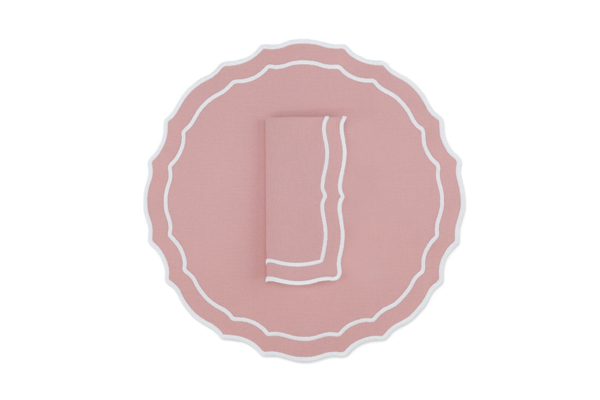 Top view of Vidro cotton-blend placemat and folded napkin set of four in dusty pink showing scalloped edge and white trim on white background
