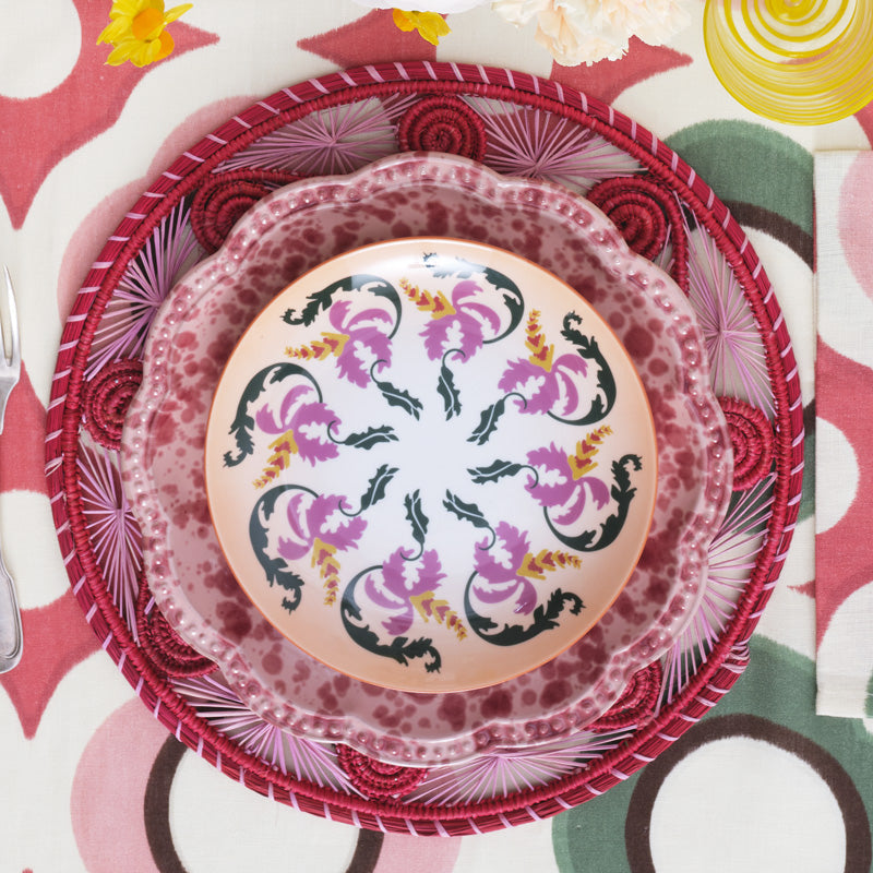 Top view of Speckled Dinner Plate in Pink showcasing its scalloped edge and decorative, undulating rim on a patterned placemat
