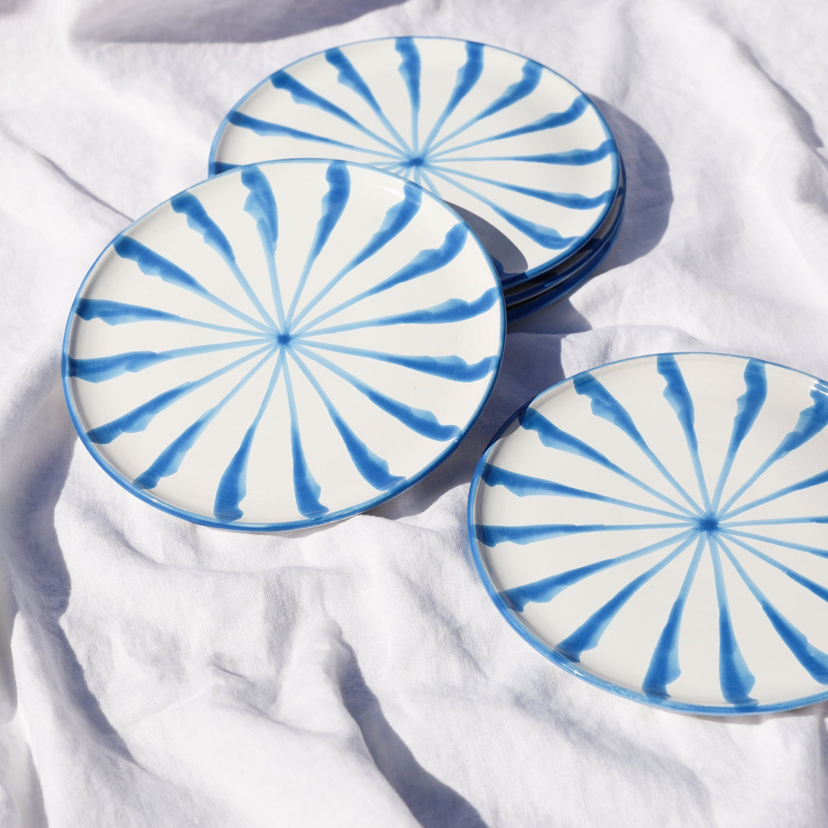 Top view of Casa Celeste salad plate showcasing blue candy cane-style radiating stripes with stacked plates on white linen