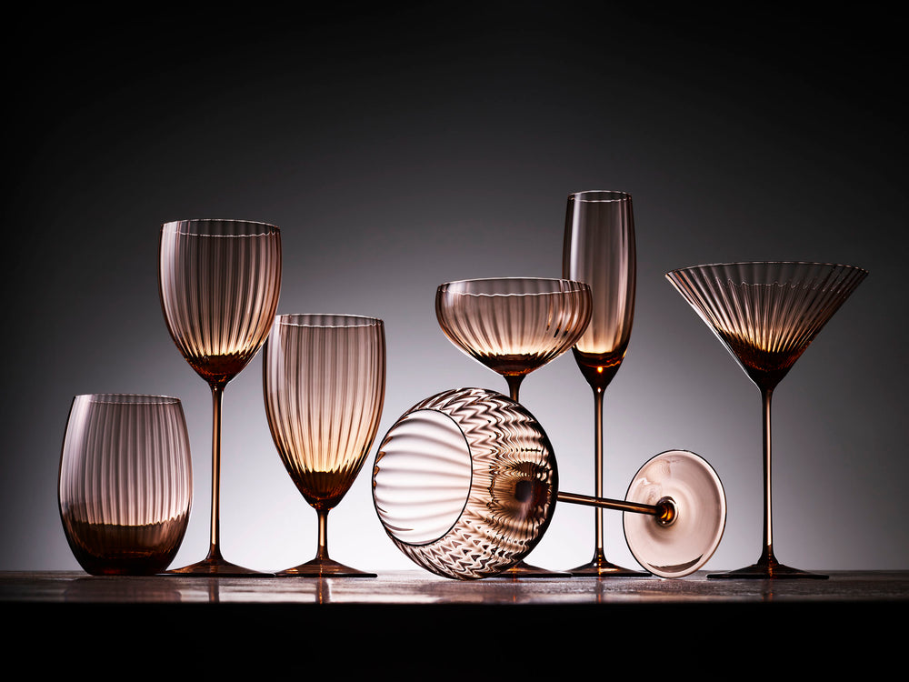 Studio grouping of Quinn Amber martini glasses (set of 2) and matching stemware showing vertical ribbed optic texture on a gray gradient background