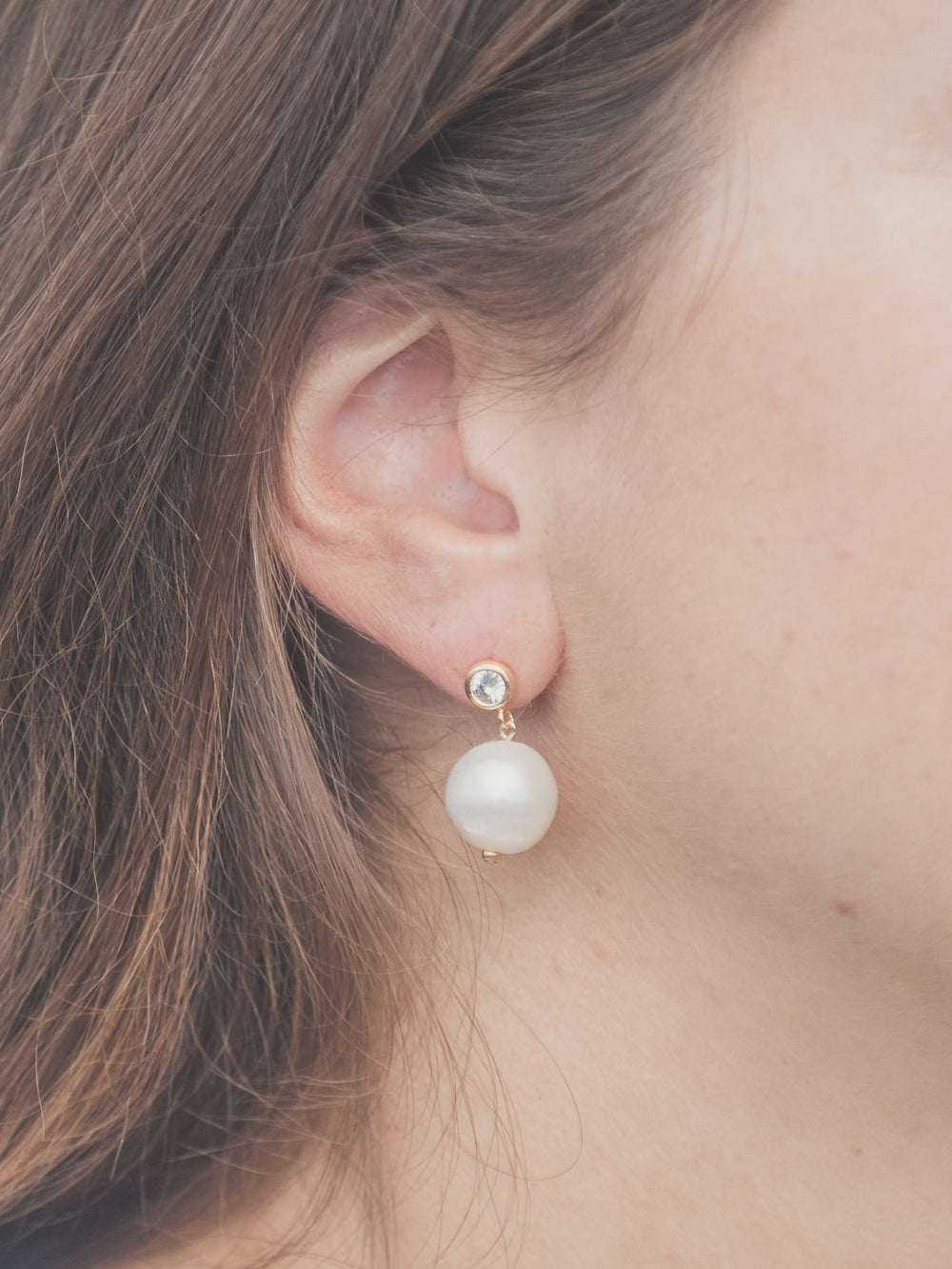 Side view of Rosamund Earrings on model showcasing gold-plated rhinestone post and dangling white freshwater pearl
