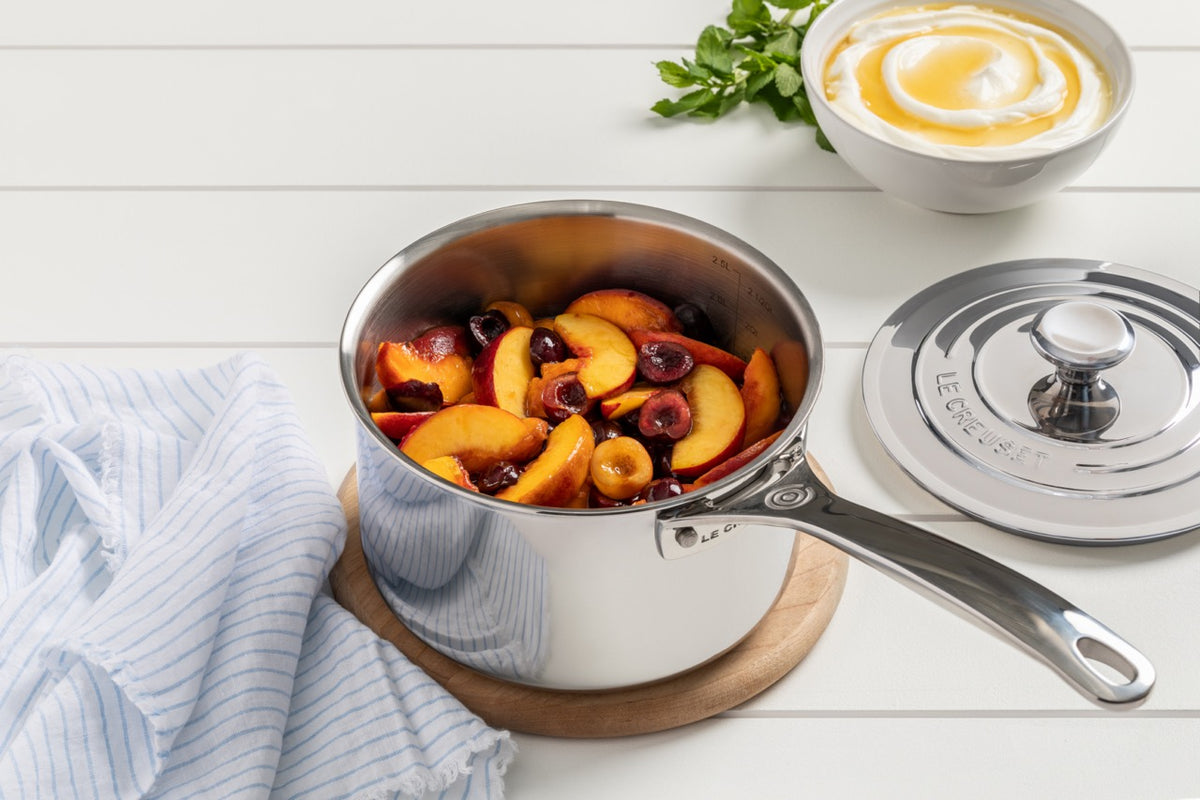 Angled view of stainless steel 3 qt saucepan with long handle and measurement marks; lid beside on white surface