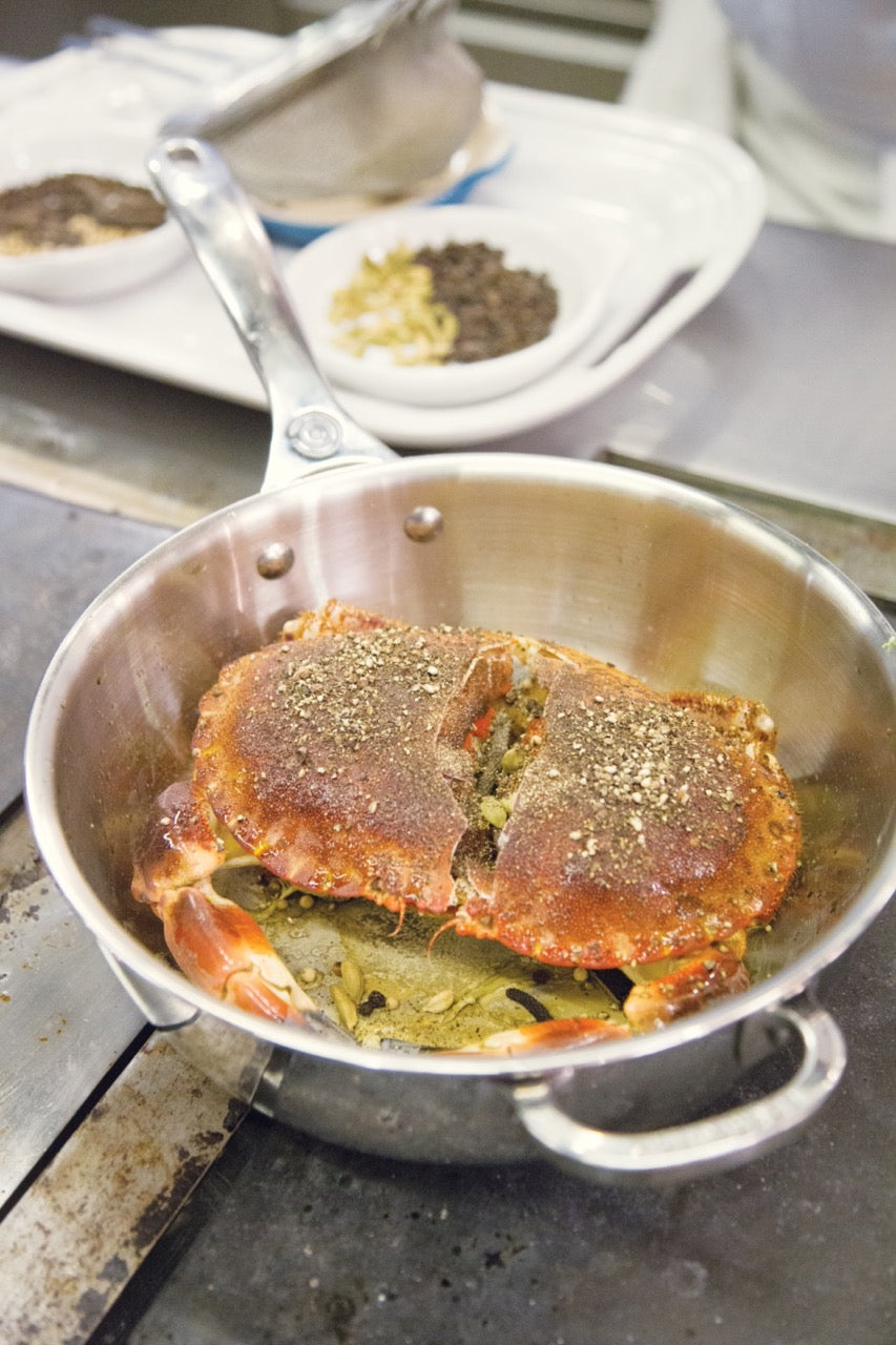 Overhead view of 3.5 qt stainless steel saucier pan showcasing cooked crab inside and helper handle on stovetop