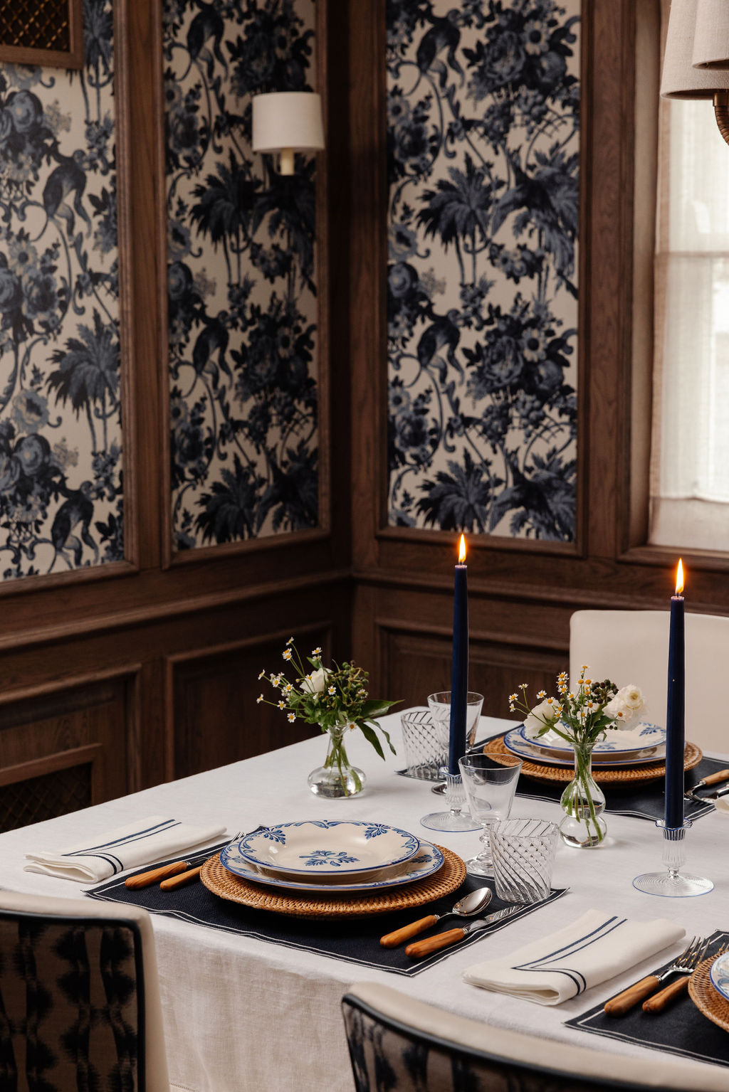 Two lit denim blue taper candles on an elegant dining table set with blue-and-white dishes and flowers