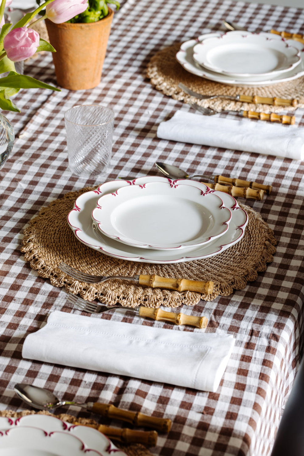 Folded white Classic Hemstitch linen napkin showing hemstitch edge on a brown gingham tablecloth at a place setting with woven placemat and bamboo-handled cutlery
