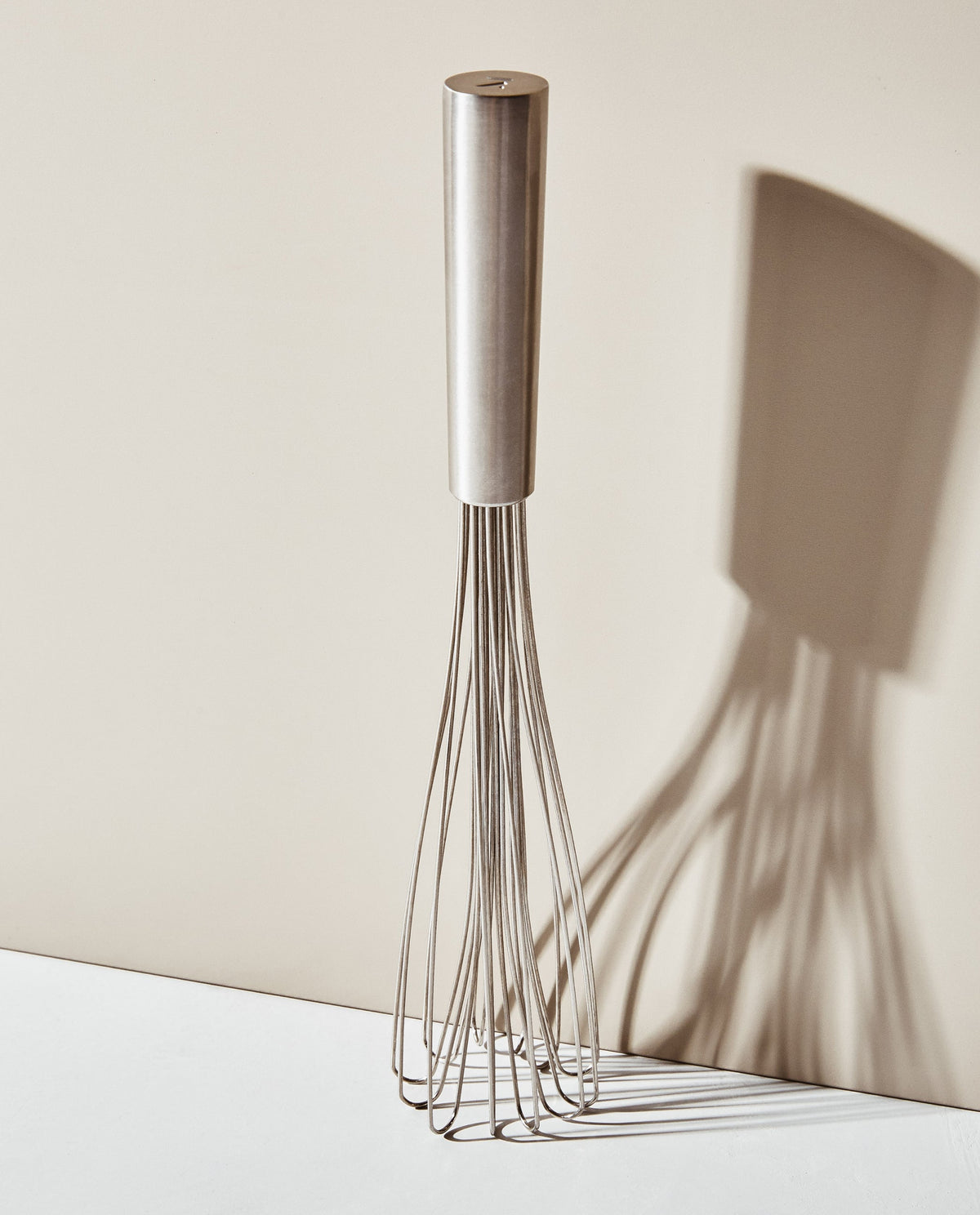Front view of The Air Whisk showcasing stainless steel wires and cylindrical handle against a neutral beige background