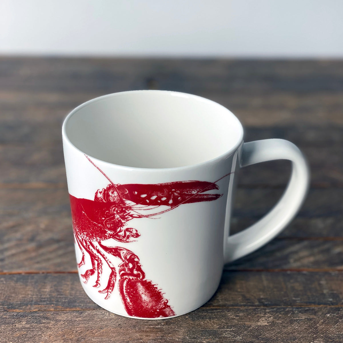 Close up view of Lobster Mug Red showcasing red lobster designs on white porcelain with a wood background