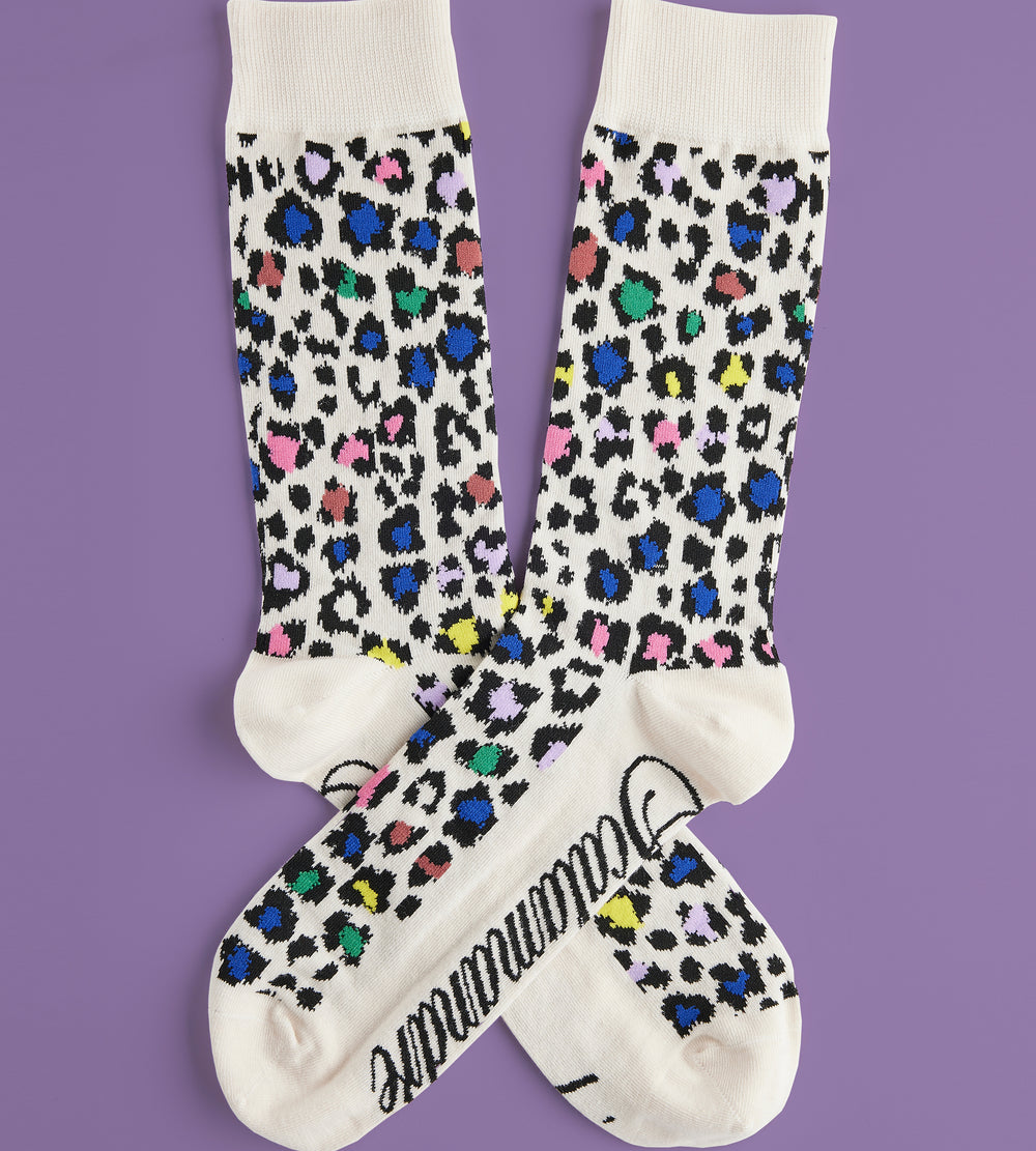 Flat-lay of Men’s Rosette socks showcasing multicolor leopard rosette pattern, cream cuffs and reinforced heel and toe on purple background