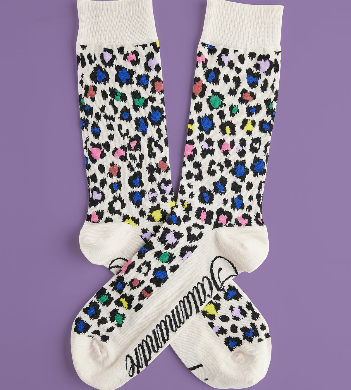 Flat-lay of Men’s Rosette socks showcasing multicolor leopard rosette pattern, cream cuffs and reinforced heel and toe on purple background