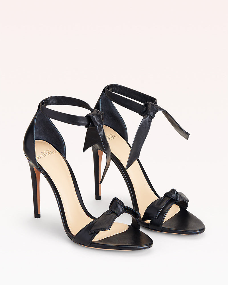 Three-quarter view of Clarita 100 in Black Leather showcasing two bow accents and stiletto heels on a white background