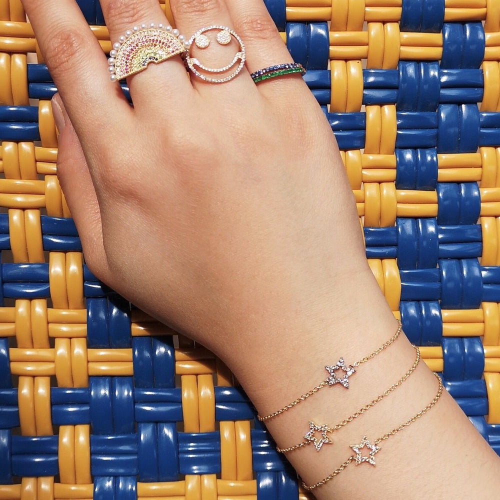 Close-up of wrist wearing three yellow gold star charm bracelets with small diamond-set stars on blue and yellow background