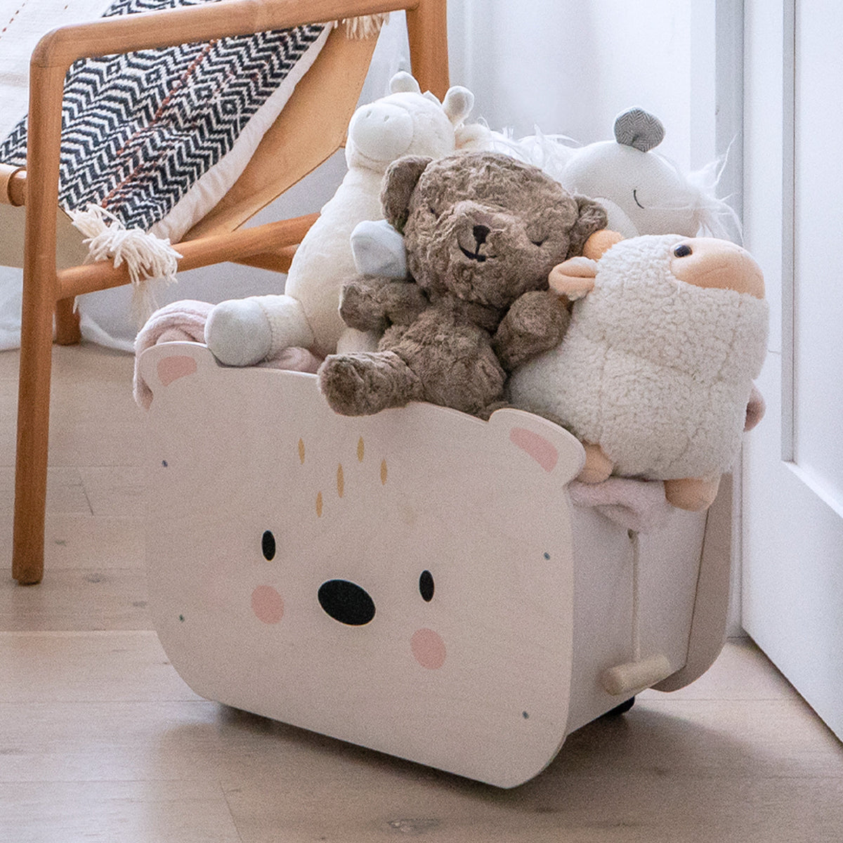 SNOObear brown plush sitting among other stuffed animals in a wooden toy box in a bright nursery