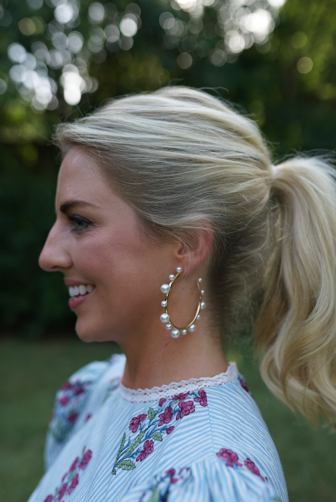 Side view of Pearl Hoops showcasing faux pearl accents on gold plated hoops with an outdoor greenery background