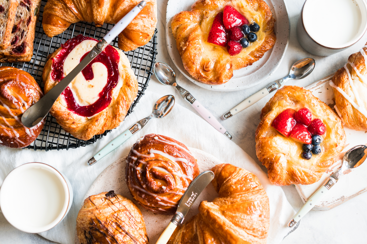 Pastel stainless steel dessert spoons arranged among pastries and coffee cups on a breakfast table